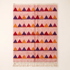 Rose Boujaad rug with horizontal sawtooth rows in crimson, purple, orange and magenta triangles, flat lay on plain background