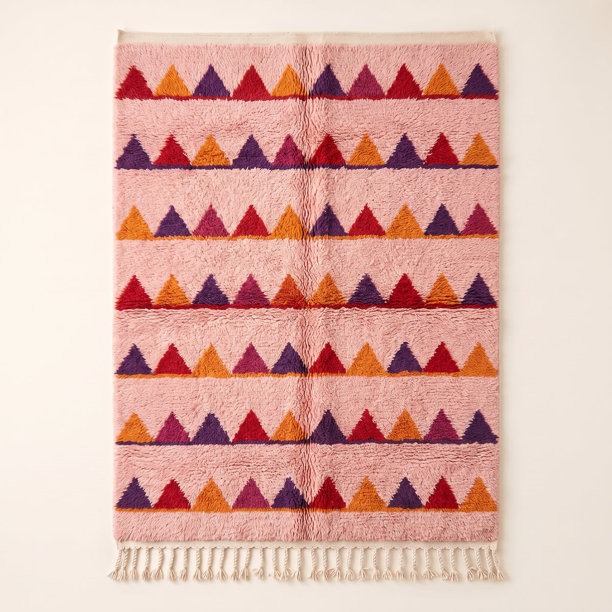 Rose Boujaad rug with horizontal sawtooth rows in crimson, purple, orange and magenta triangles, flat lay on plain background