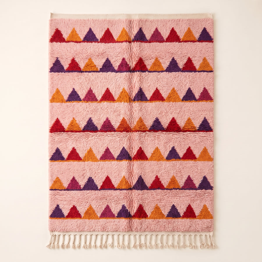 Rose Boujaad rug with horizontal sawtooth rows in crimson, purple, orange and magenta triangles, flat lay on plain background
