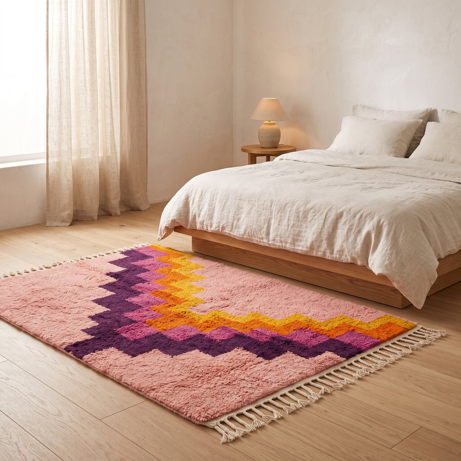 Tamuli rug in bedroom setting beside wooden bed with cream bedding, showing stair-step pattern
