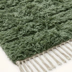 Texture detail of sage green rug pile with cream wool strands and hand-knotted surface