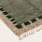 Angled view of the Ifru sage green, forest green and ivory Beni Ourain rug showing the block border design.