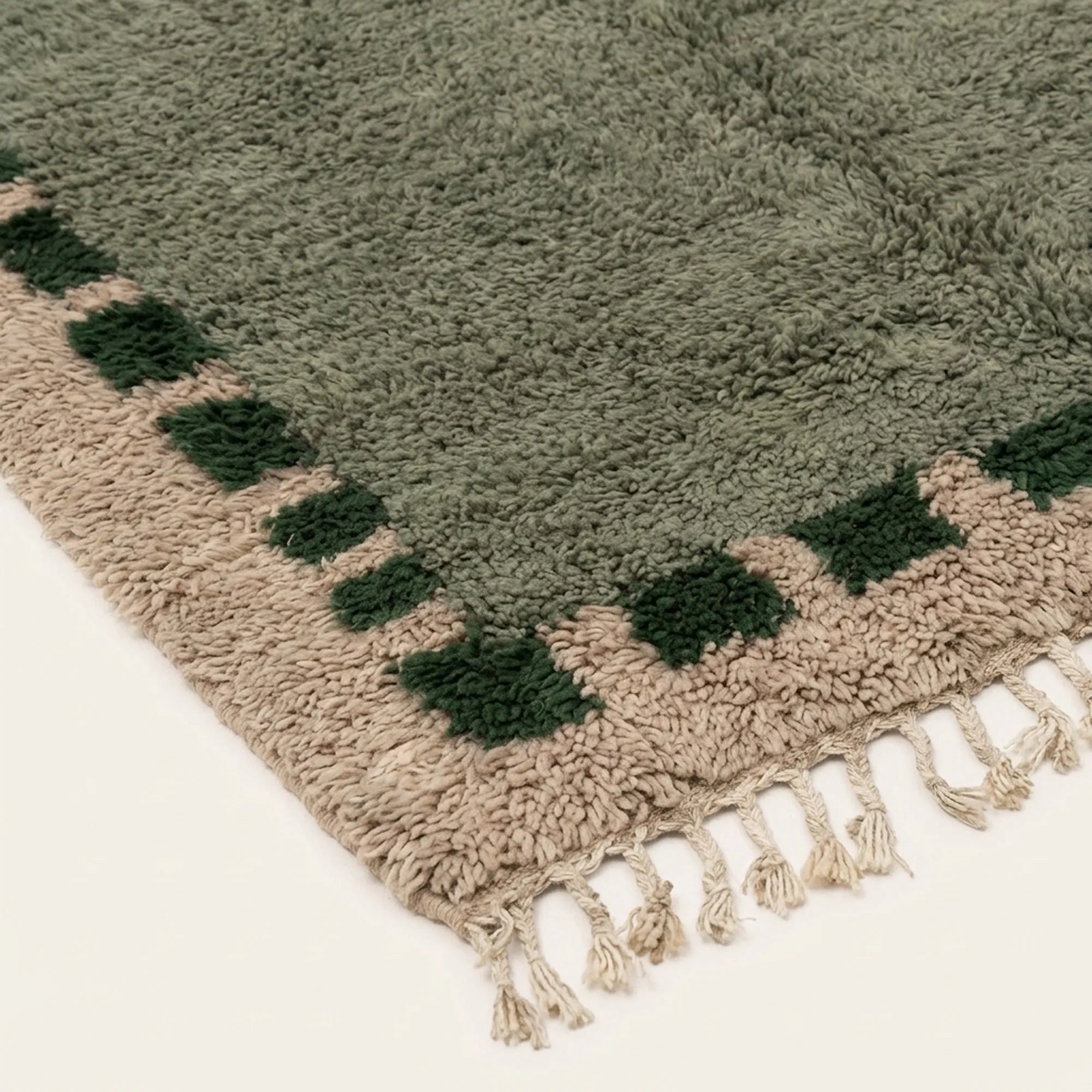 Angled view of the Ifru sage green, forest green and ivory Beni Ourain rug showing the block border design.