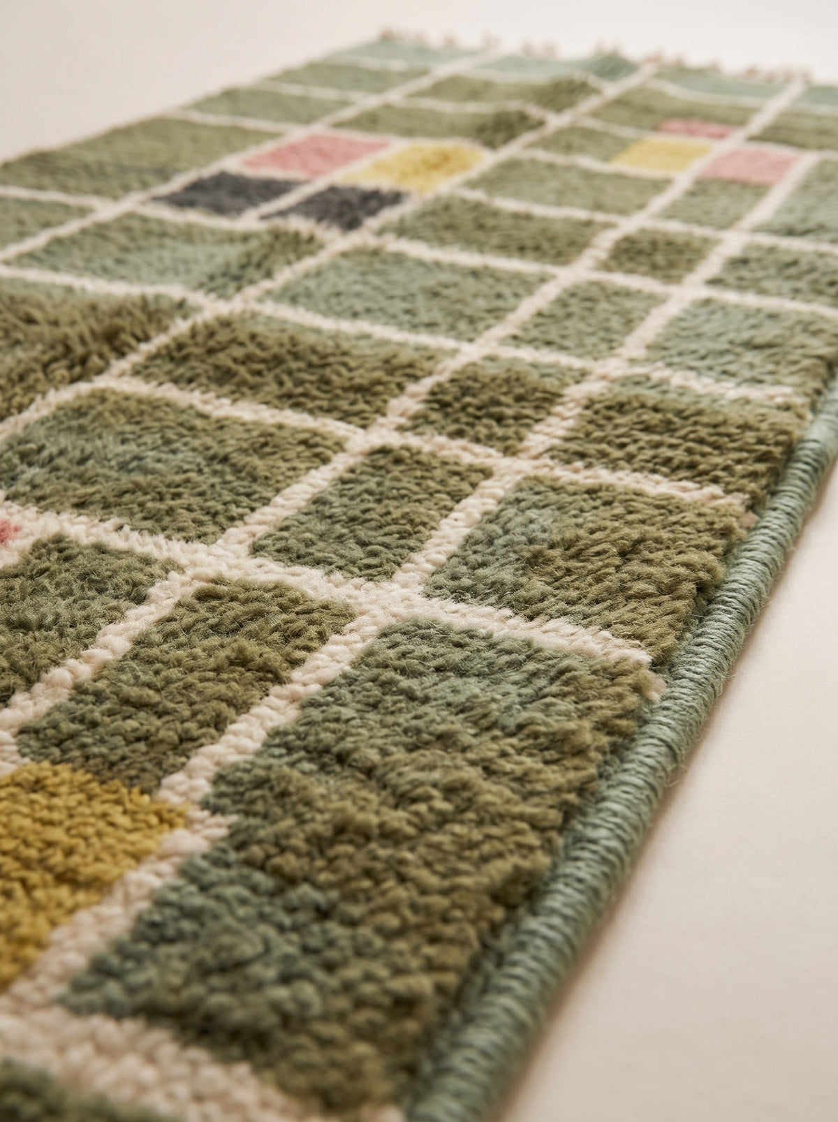 Close-up of the plush hand-knotted pile showing sage green, olive, and cream grid check blocks with pink and mustard accents