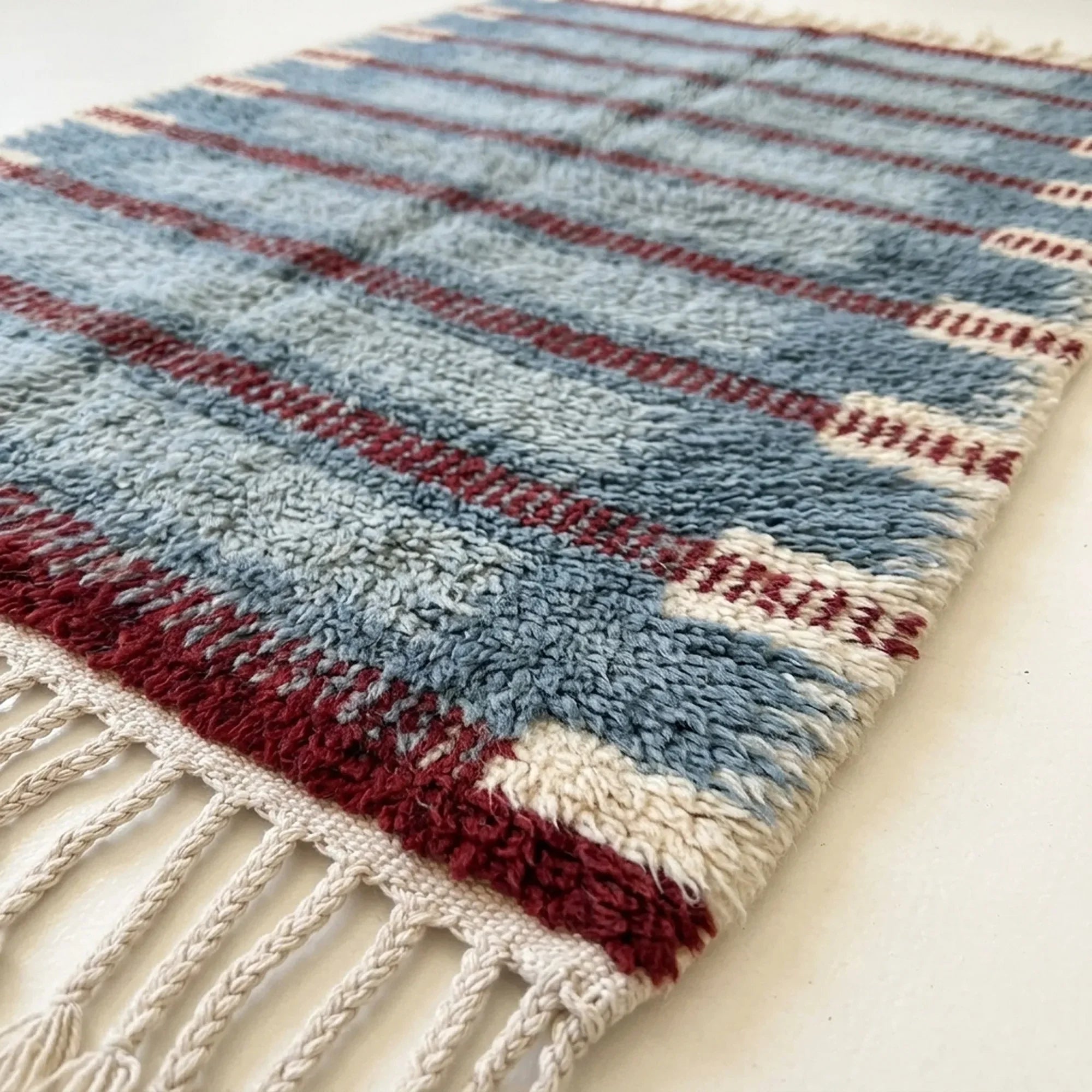 Close-up of the slate blue and burgundy horizontal band pattern on the Izen ivory wool rug.