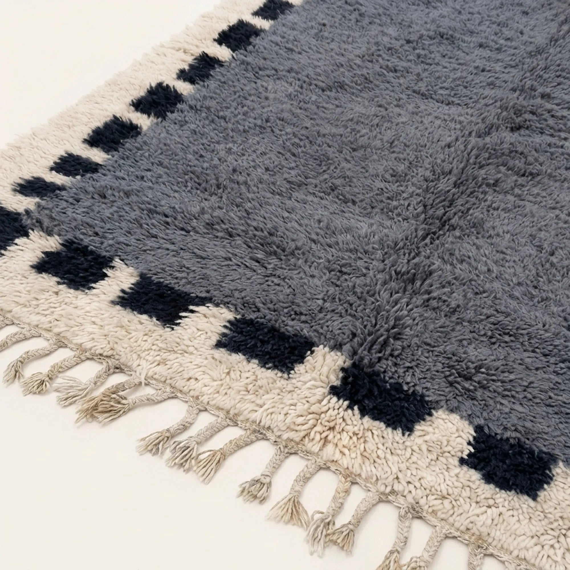 Angled view of the Tamesna slate blue, navy and ivory Beni Ourain rug showing the block border design.