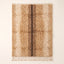 Tan and chocolate Beni Ourain rug with scattered ivory spots, flat lay on plain background