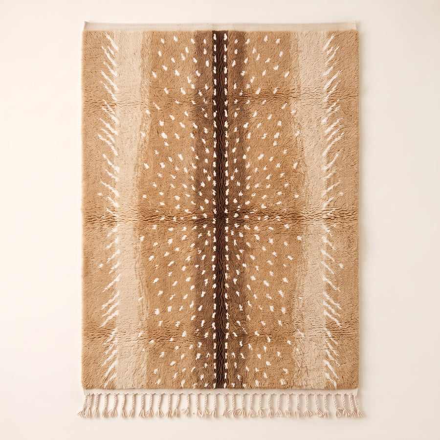 Tan and chocolate Beni Ourain rug with scattered ivory spots, flat lay on plain background
