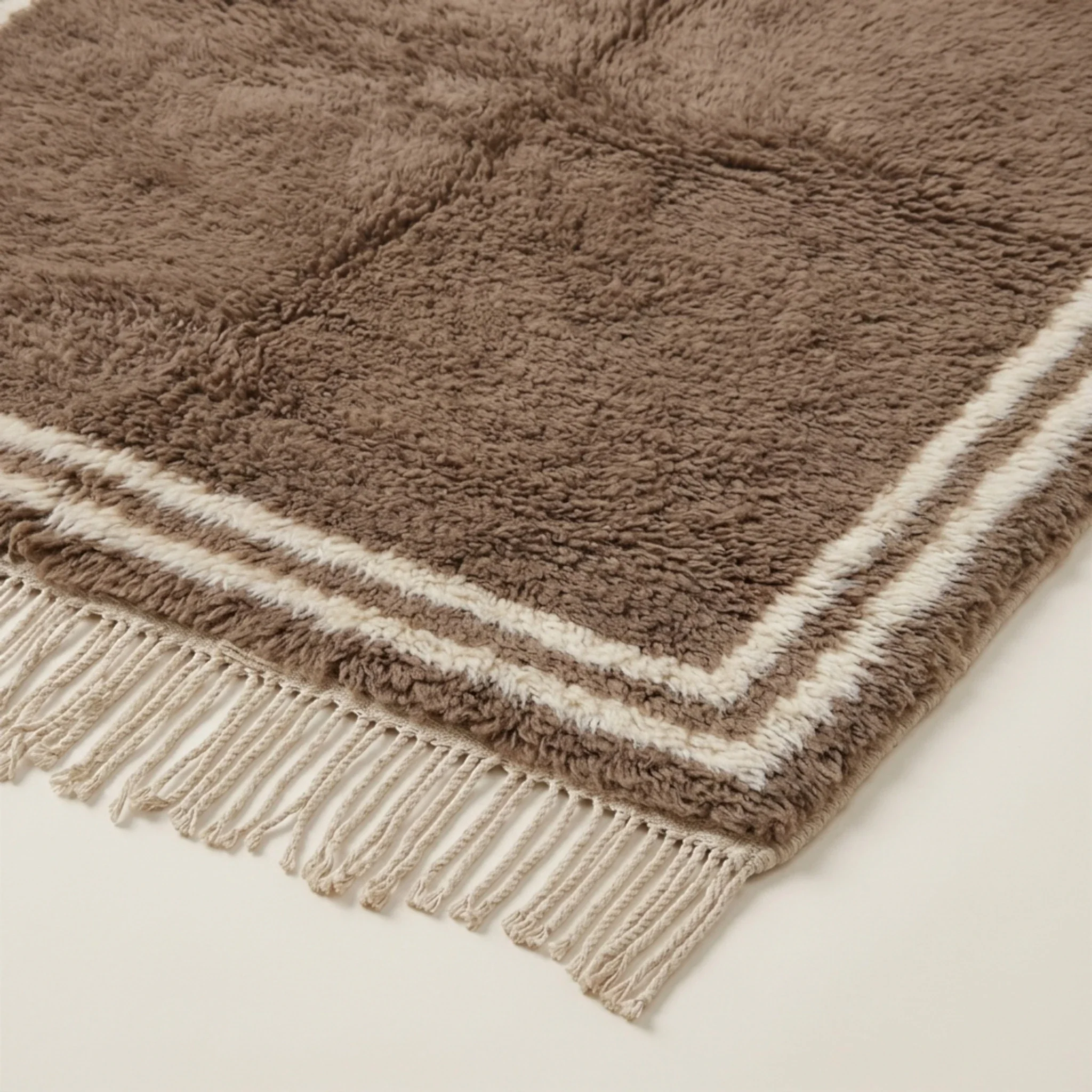 Corner and hand-tied fringe detail of the Ayyur taupe and ivory wool rug.
