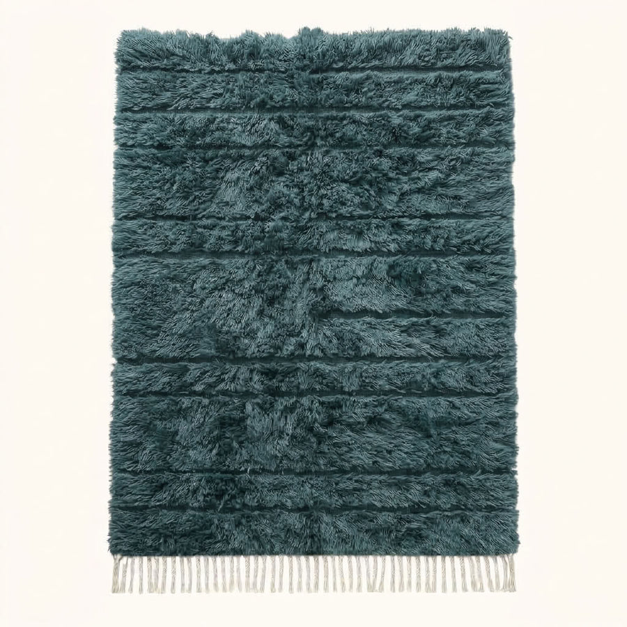 Full view of teal Beni Ourain rug with diamond lattice pattern and cream fringe on plain background