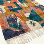 Angled view of Tazmara showing teal, coral and ochre patchwork shapes and wool fringe