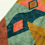 Close-up of the Tifawin Boujaad rug showing plush teal wool pile surrounding a coral geometric inset