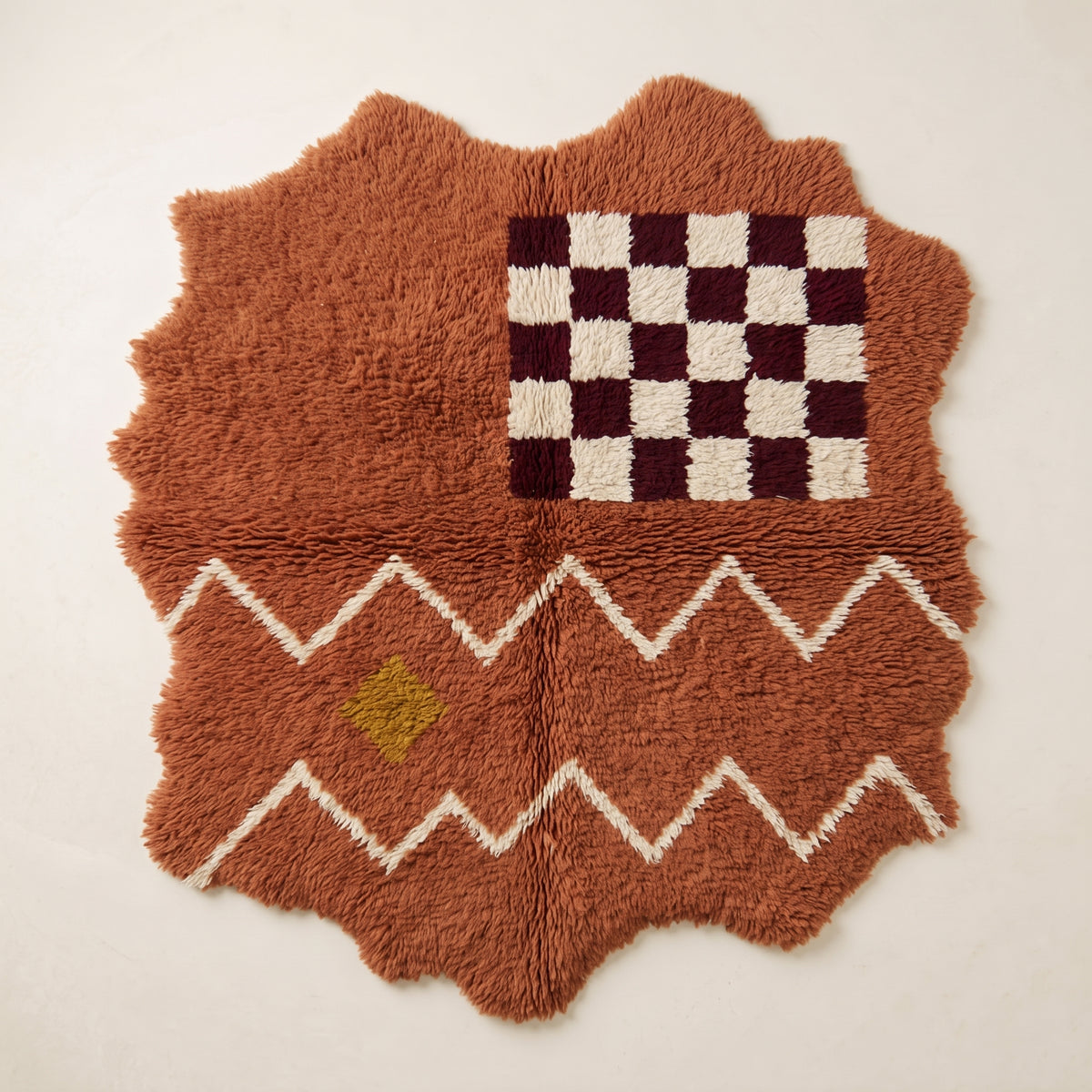 Terracotta Azilal rug with scalloped edges, featuring a burgundy and ivory checkerboard panel at the top, white zigzag bands, and a small golden-yellow diamond accent below