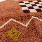 Close-up of terracotta wool pile and ivory zigzag band showing handwoven texture detail