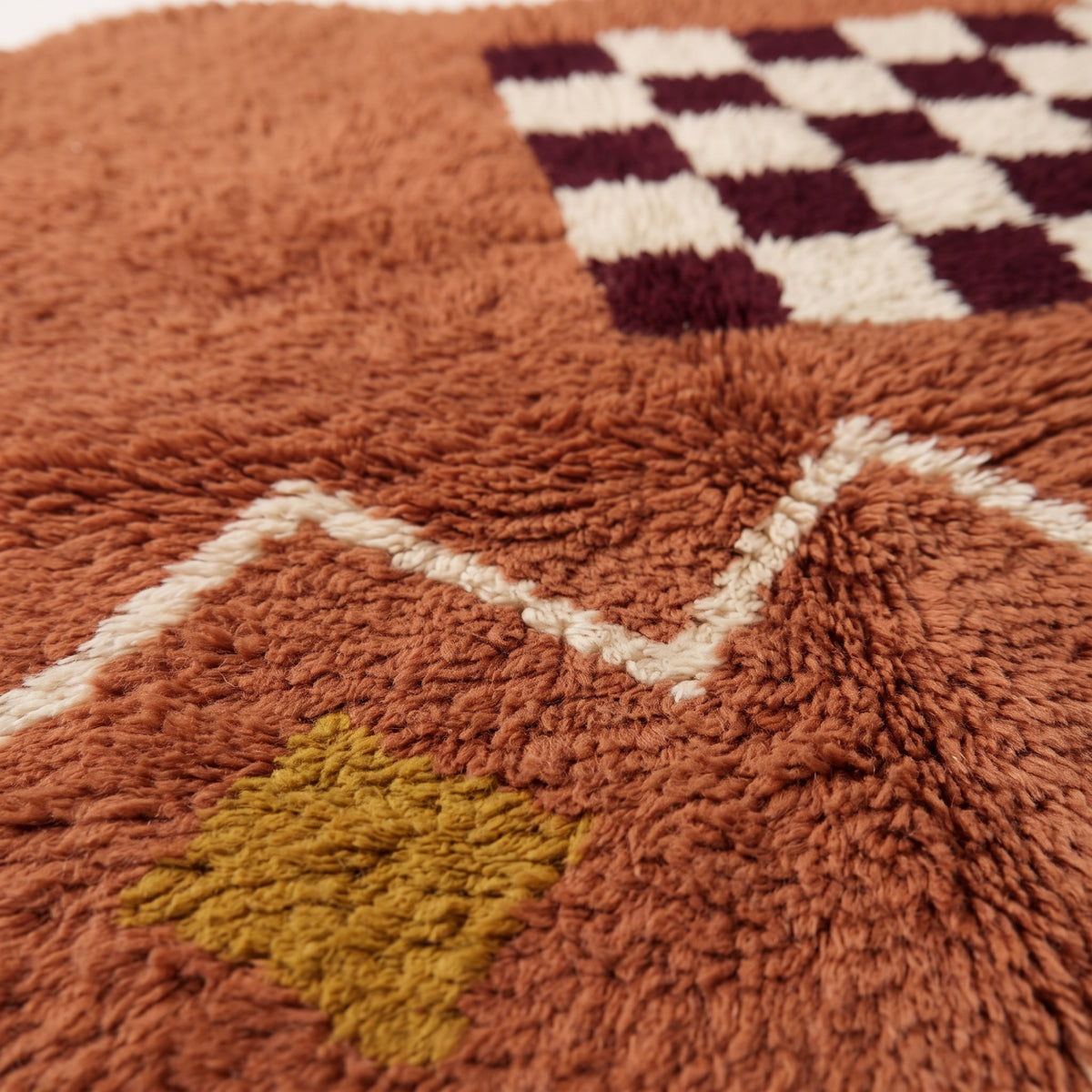 Close-up of terracotta wool pile and ivory zigzag band showing handwoven texture detail