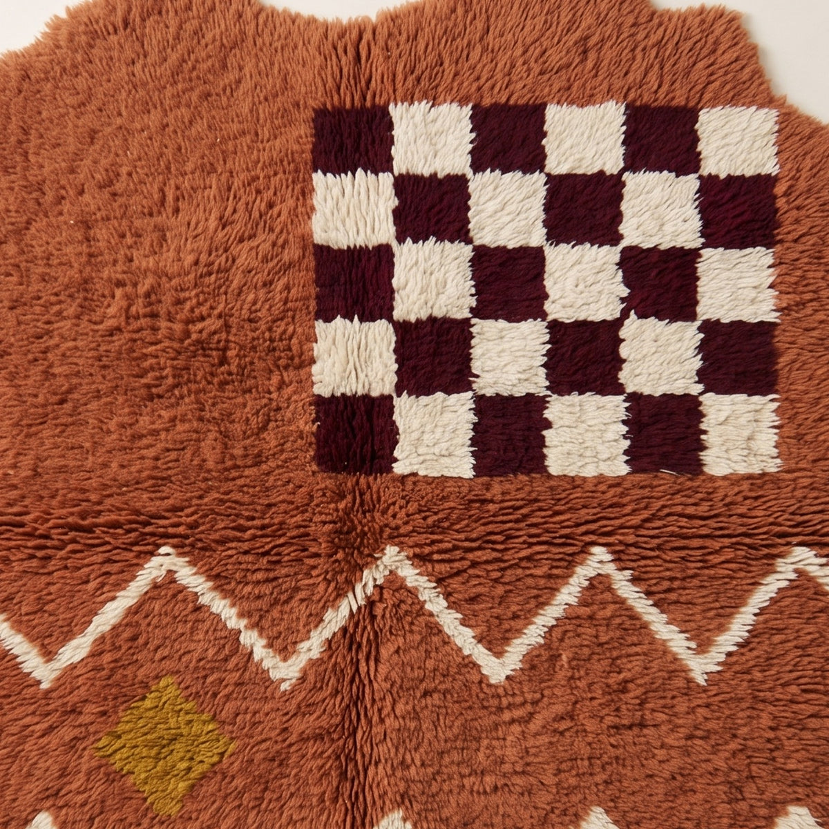 Terracotta rug corner showing scalloped edge with zigzag band and burgundy checkerboard panel