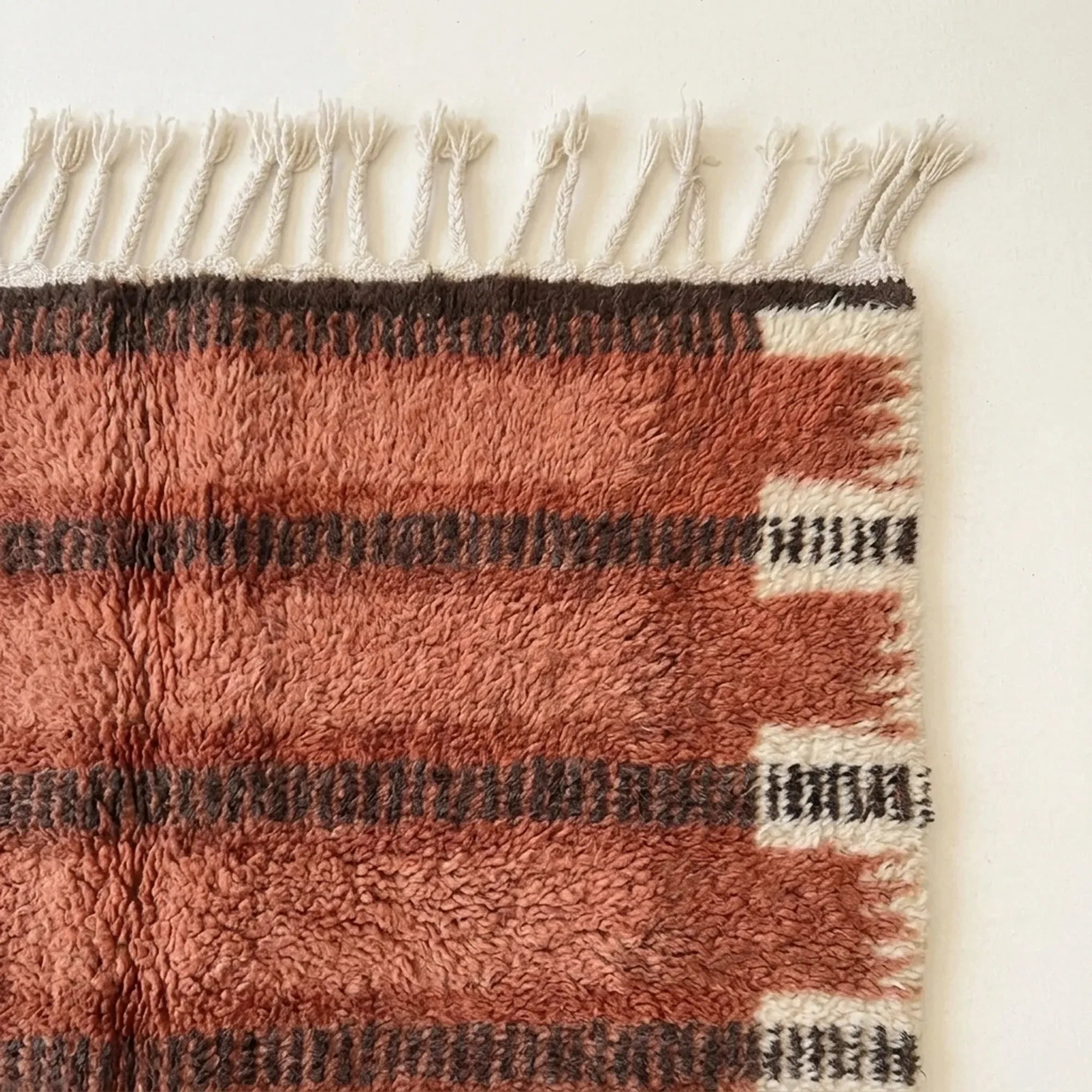 Angled view of the Tiziri terracotta, charcoal and ivory hand-knotted Beni Ourain rug.