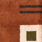 Corner detail of Mrirt rug showing pinstripe pattern at top and patchwork blocks with olive square