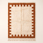 Terracotta and ivory Beni Ourain rug with crenellated battlement border on plain background, flat lay
