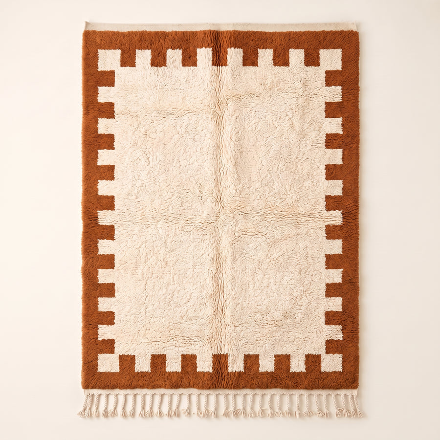 Terracotta and ivory Beni Ourain rug with crenellated battlement border on plain background, flat lay