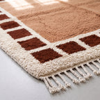 Corner detail of Tafat rug showing checkered border in terracotta and cream with fringe edge