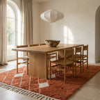 Terracotta and ivory diamond lattice Beni Ourain rug in bright dining room under wooden table with woven chairs