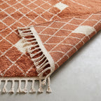 Close-up of edge and fringe on terracotta and ivory diamond lattice rug, showing handwoven construction and twisted tassel fringe