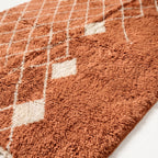 Close-up of handwoven terracotta wool pile with cream diamond lattice lines and ivory accent diamond, showing texture and depth