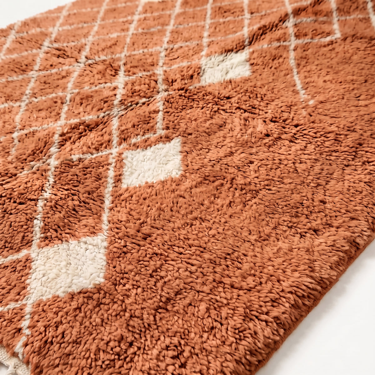 Close-up of handwoven terracotta wool pile with cream diamond lattice lines and ivory accent diamond, showing texture and depth