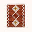 Terracotta and ivory Beni Ourain rug with diamond lattice and mustard cross design, flat lay on plain background