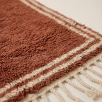 Close-up of the double border texture on the Tislit terracotta and ivory wool rug.