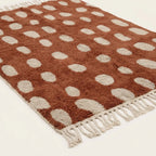 Angled view of the Agdal terracotta and ivory Beni Ourain rug showing the oval grid design.