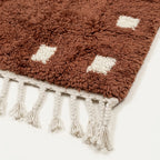 Handmade texture and edge detail of the terracotta and ivory wool rug.