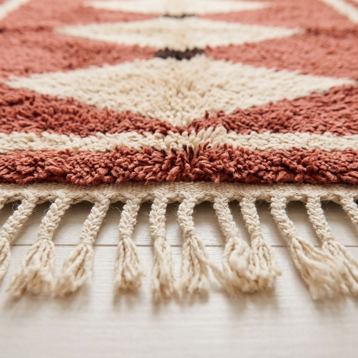Close-up of pile texture showing dense hand-knotted wool in terracotta, ivory and cream with fringe