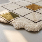 Angled view of Beni Ourain rug pile showing olive and ivory squares with gold diamond centre and dark brown lines