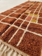 Close-up of plush pile showing terracotta, rust, mustard and cream wool with grid check structure and texture
