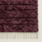 Bottom edge detail of wine Beni Ourain rug showing cream wool fringe against dark pile